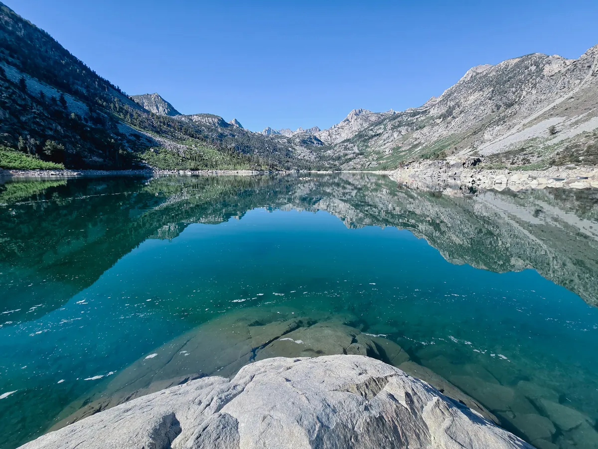 Clear alpine lake mirroring granite peaks under a blue sky