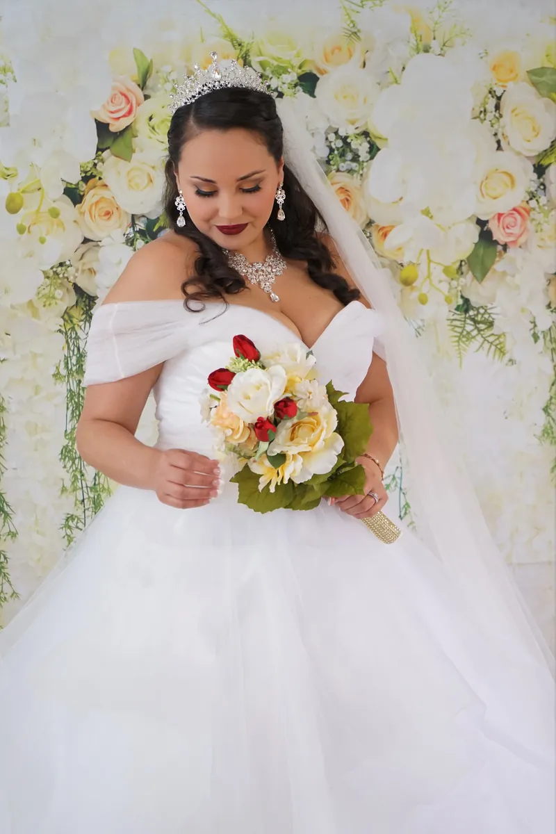 Bride in a tiara looking down at her bouquet of ivory and red roses