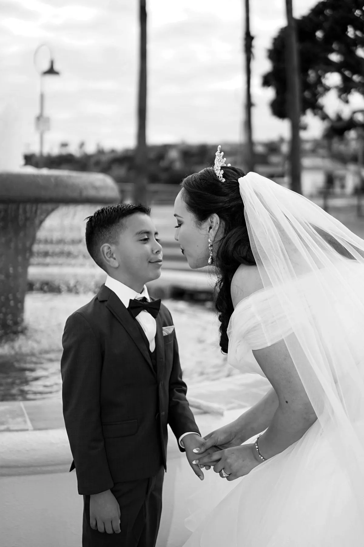 Black and white photo of a bride leaning down to a young boy in a tuxedo