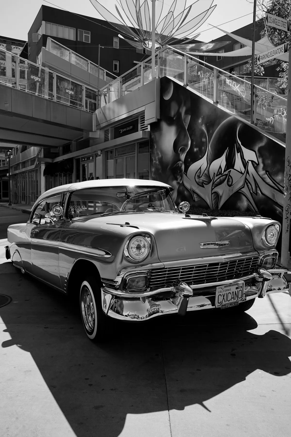 Black and white photo of a 1950s classic car parked beneath a mural