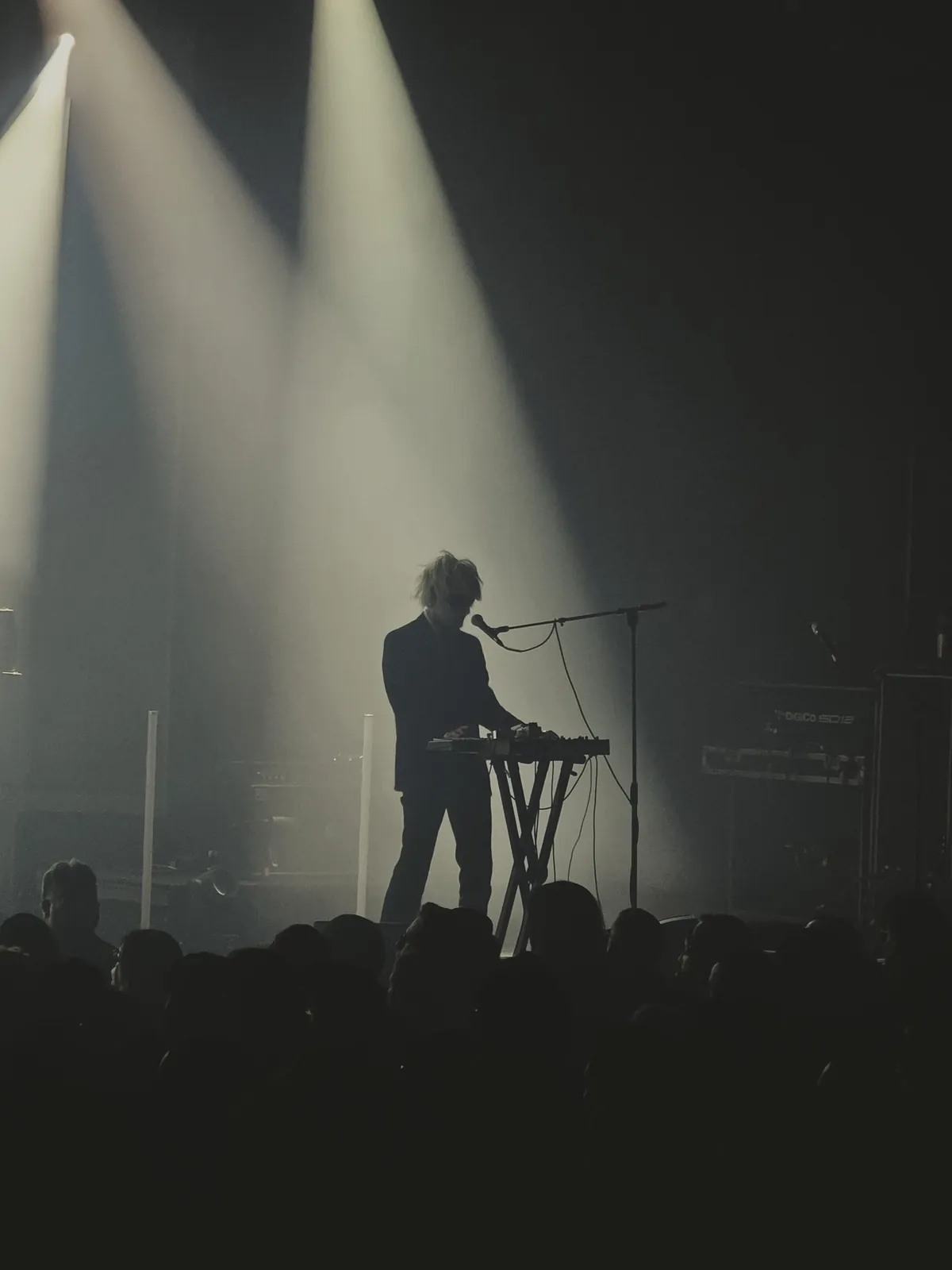 Silhouette of a musician at a keyboard beneath beams of stage light