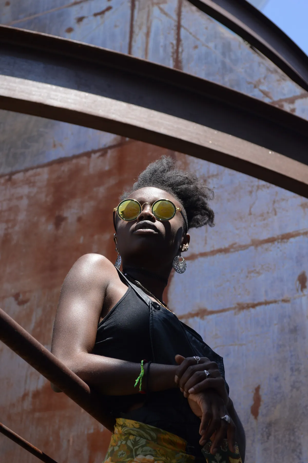 Low-angle portrait of a model in gold sunglasses against a weathered blue wall