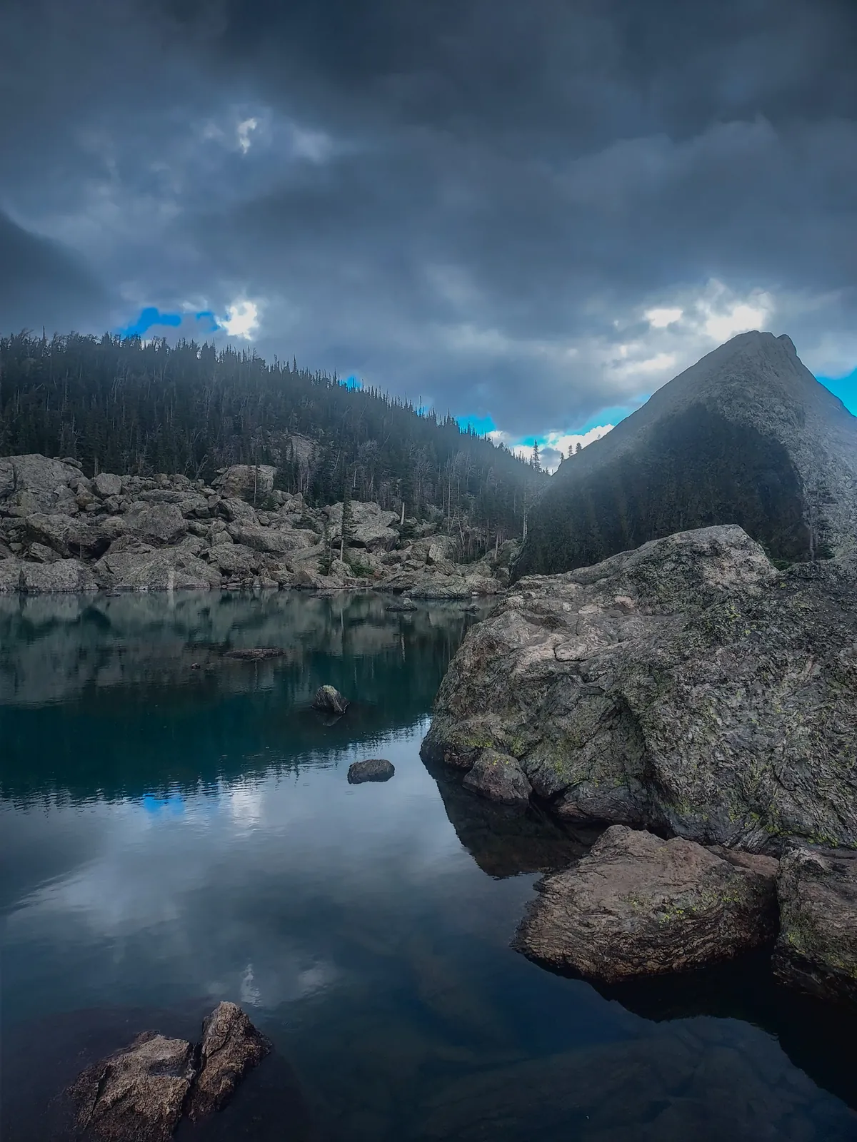 Mountain lake with boulders under dark storm clouds