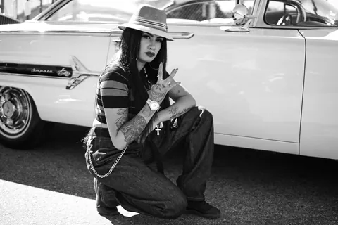 Black and white portrait of a woman in a wide-brim hat crouched beside a classic car