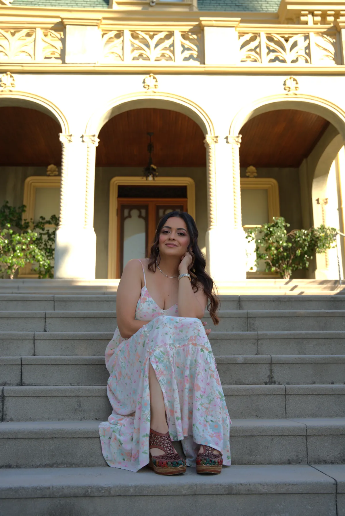 Woman in a floral sundress seated on the steps of a historic mansion