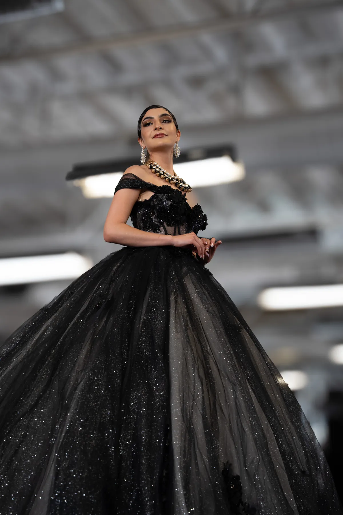 Model in a black ball gown and gold jewelry on the runway