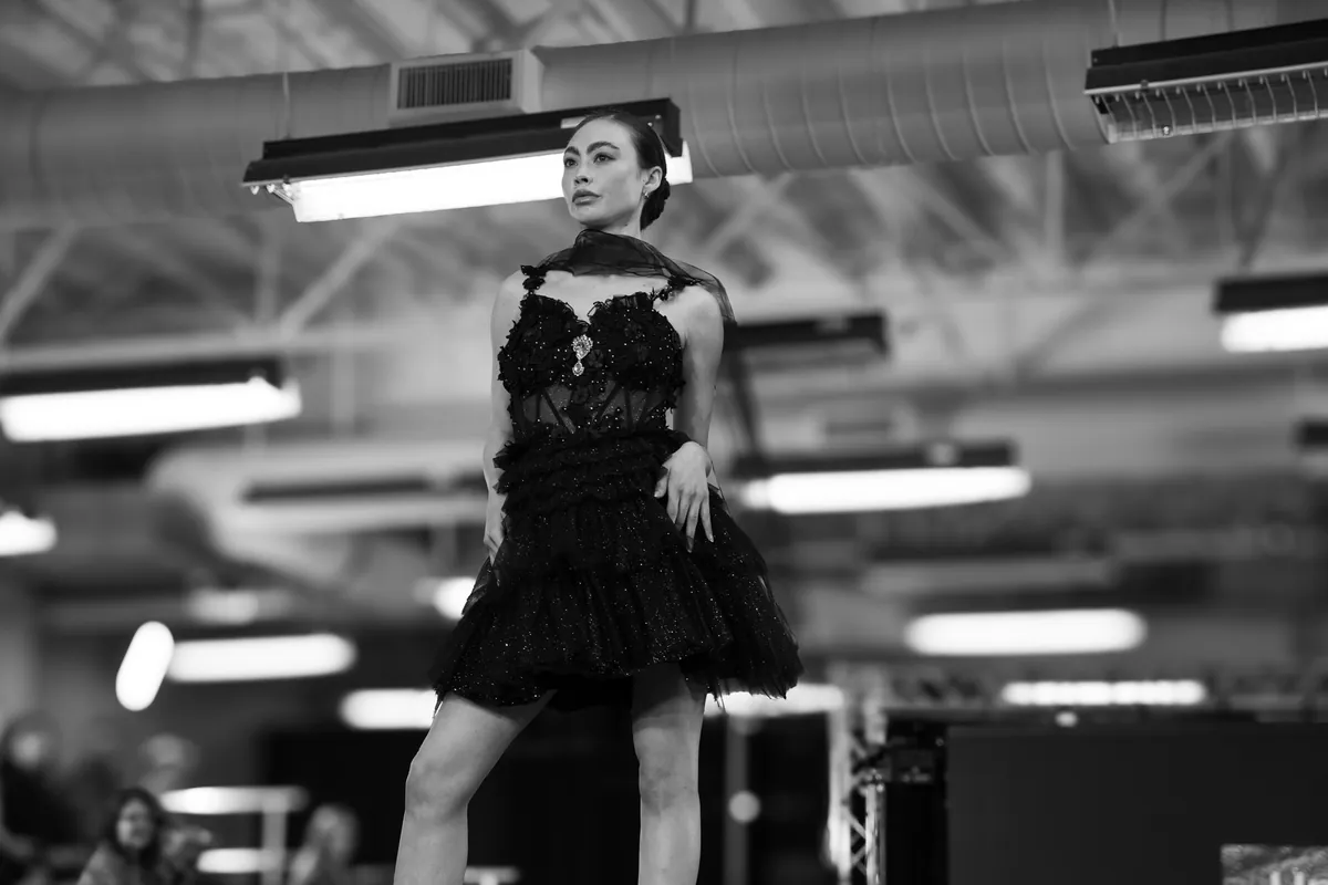 Black and white photo of a model in a black tulle dress on the runway