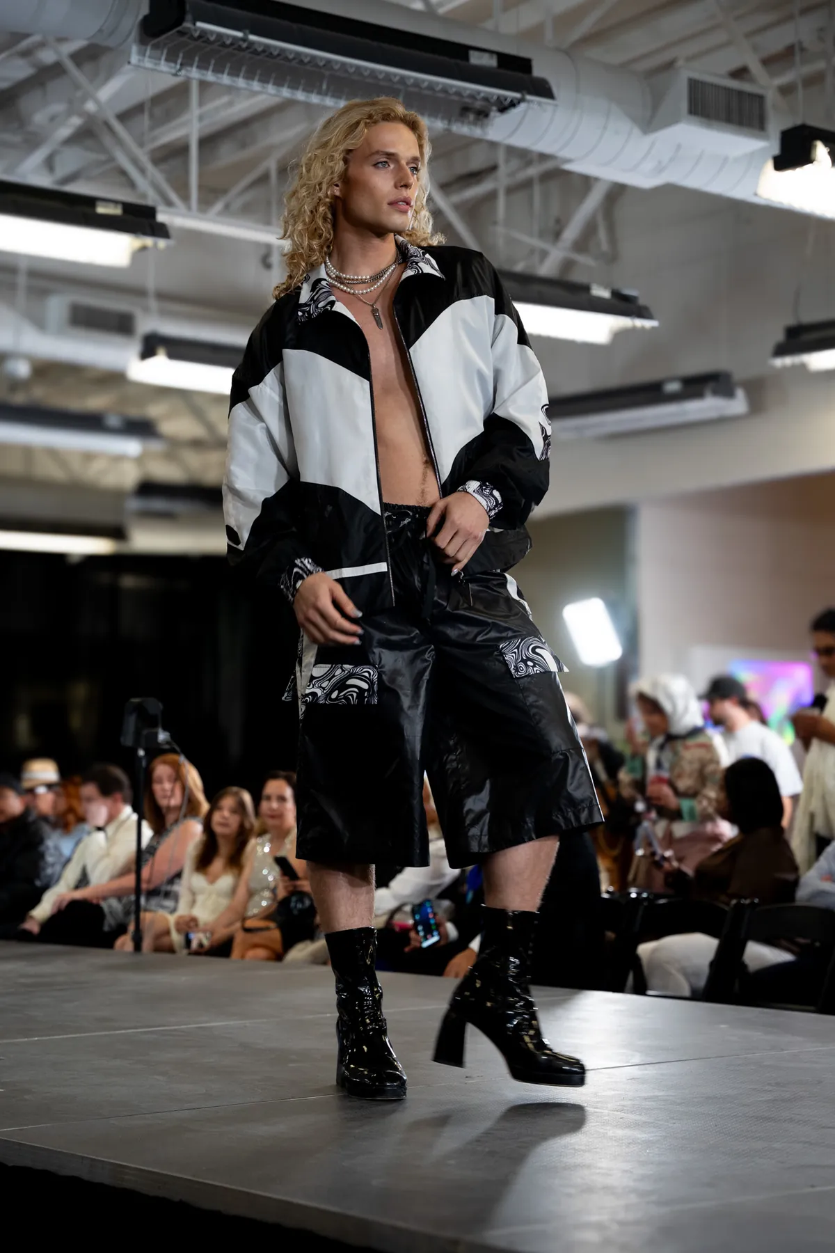 Model in a black and white jacket and shorts walking a runway