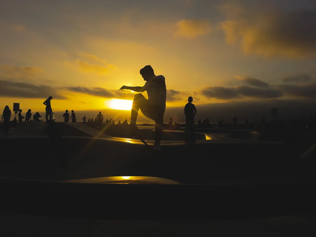 Skateboarder silhouetted against a sunset at a skatepark