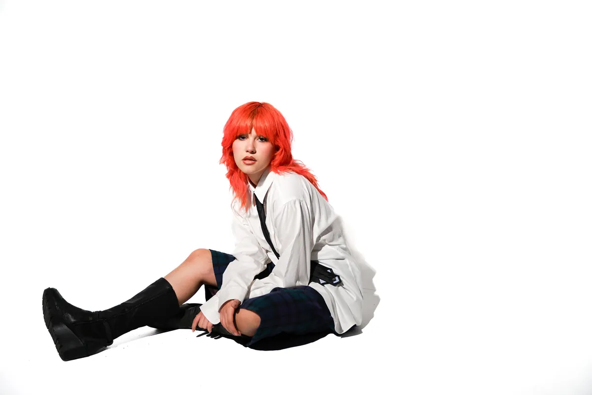 Model with bright red hair seated on a white studio backdrop
