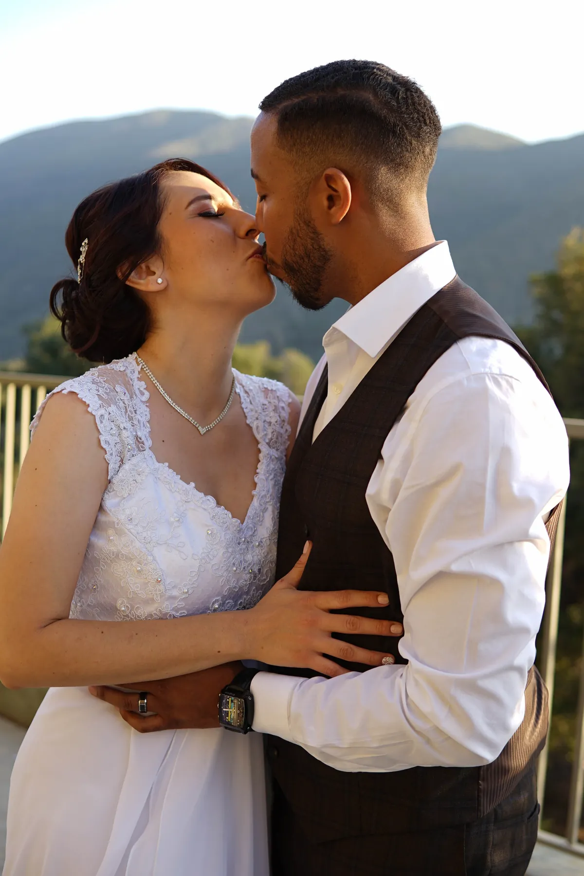 Newlyweds kissing on a balcony with mountains behind them